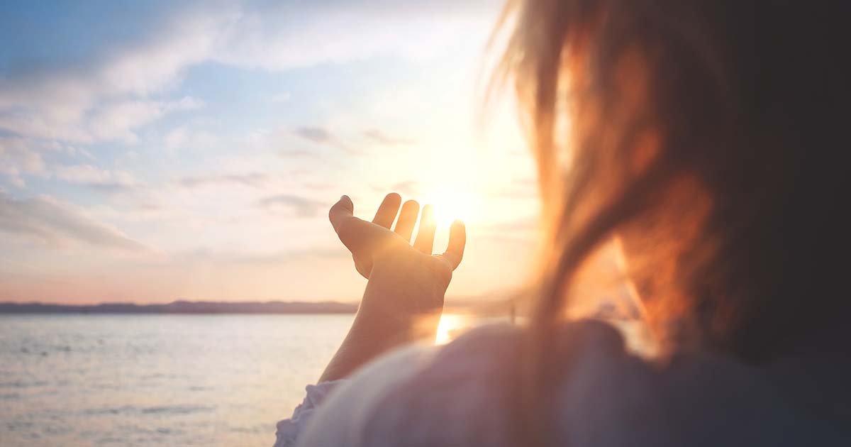 Woman watching sunrise and raising a hand towards the Sun.