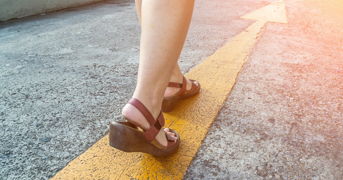 Close up of woman's lower legs wearing sandals walking on a yellow arrow on the road.
