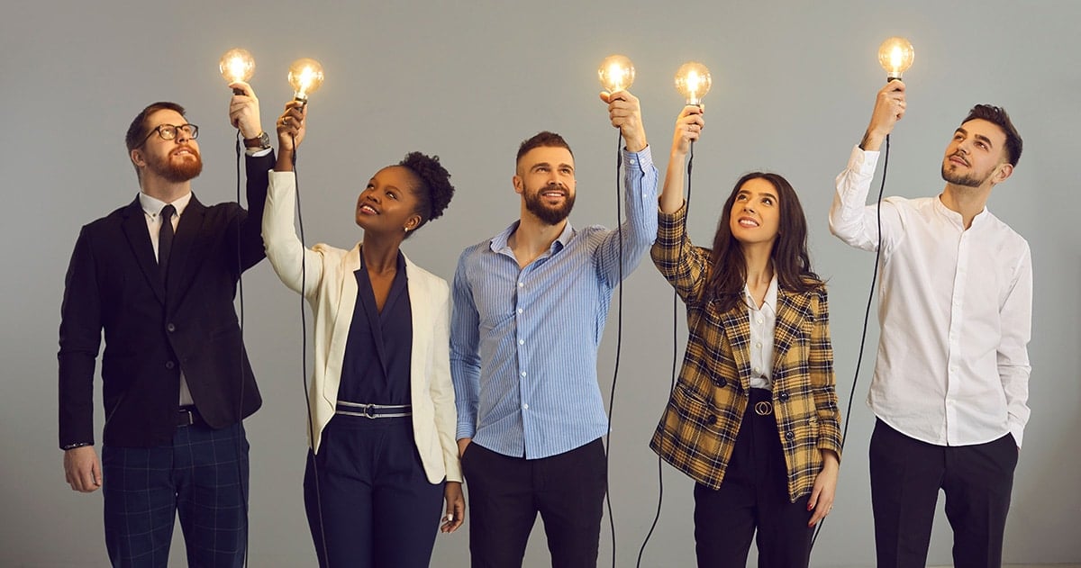 Three men and two women holding up light bulbs that are lit and looking up at the light bulbs.