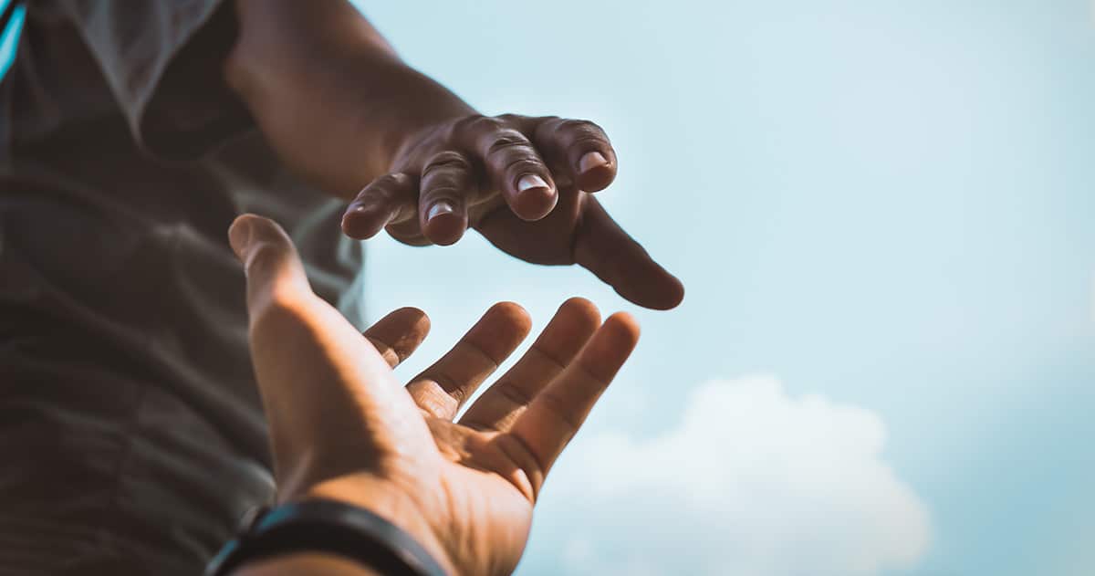 Close up of two hands with one hand helping grab another person's hand while climbing.