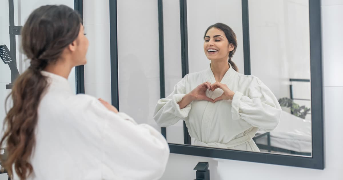 Woman looking in the mirror making a heart shape with her hands.
