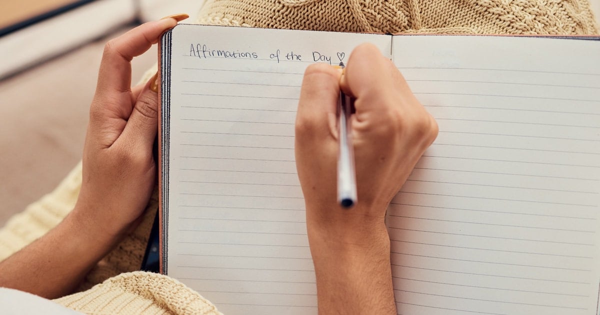 Close up of woman's hands writing affirmations in a notebook.